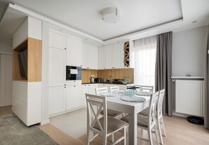 Une cuisine moderne avec des meubles blancs, une table à manger avec des chaises et un four encastré.