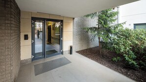 A building entrance with a glass door, a small outdoor area with a tree, and a brick wall. - Bielany Spacious Apartment (Warszawa)