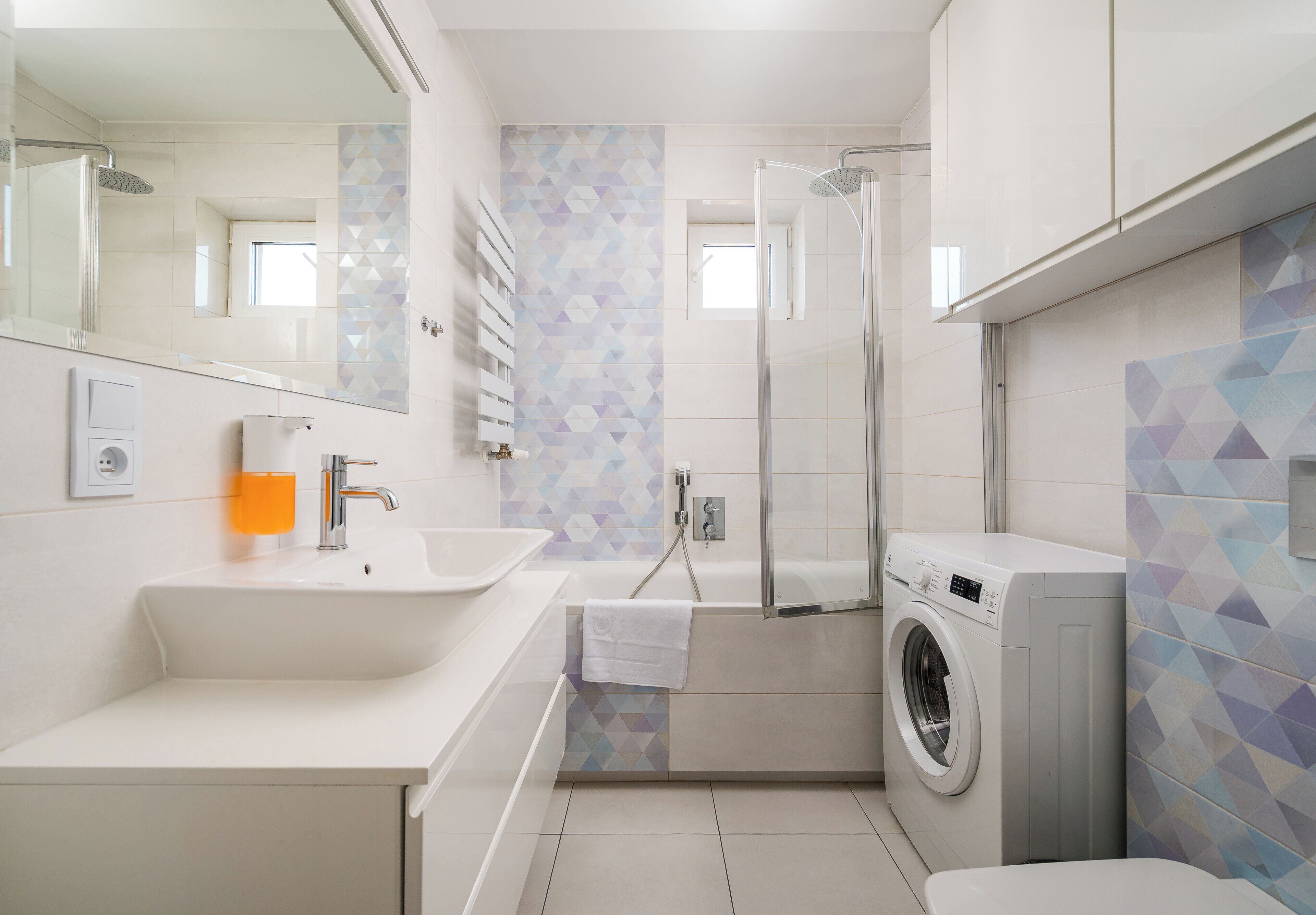 Un baño moderno con lavamanos, espejo, ducha y lavadora.