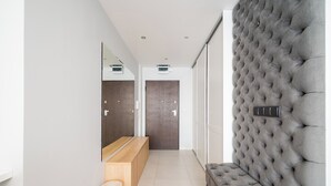 A modern hallway with a tufted headboard, a wooden bench, a mirror, and a door. - Bielany Spacious Apartment (Warszawa)