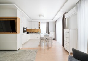 Une cuisine moderne avec des meubles blancs, un coin repas comprenant une table et des chaises, et un canapé gris.