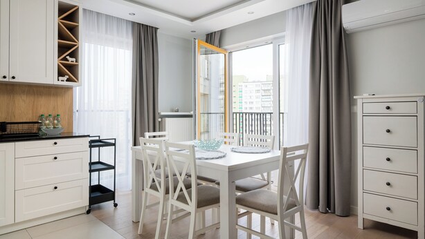 A modern kitchen with white cabinetry, a dining table with chairs, and a view of the city through large windows. - Bielany Spacious Apartment (Warszawa)