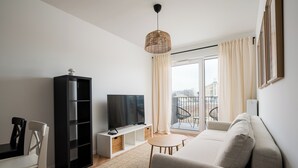 A modern living room with a sofa, TV, bookshelf, and a balcony with a chair. - Hemara Modern Apartment (Warszawa)