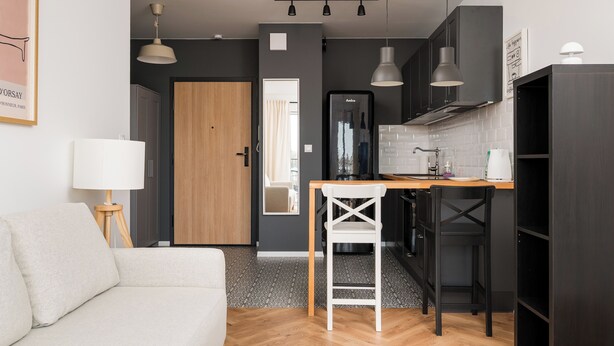 A modern kitchen with a wooden countertop, a white chair, and a black hanging light fixture. - Hemara Modern Apartment (Warszawa)
