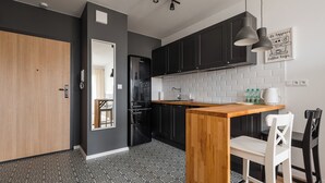 A modern kitchen with dark cabinets, a wooden island, and a white chair. - Hemara Modern Apartment (Warszawa)