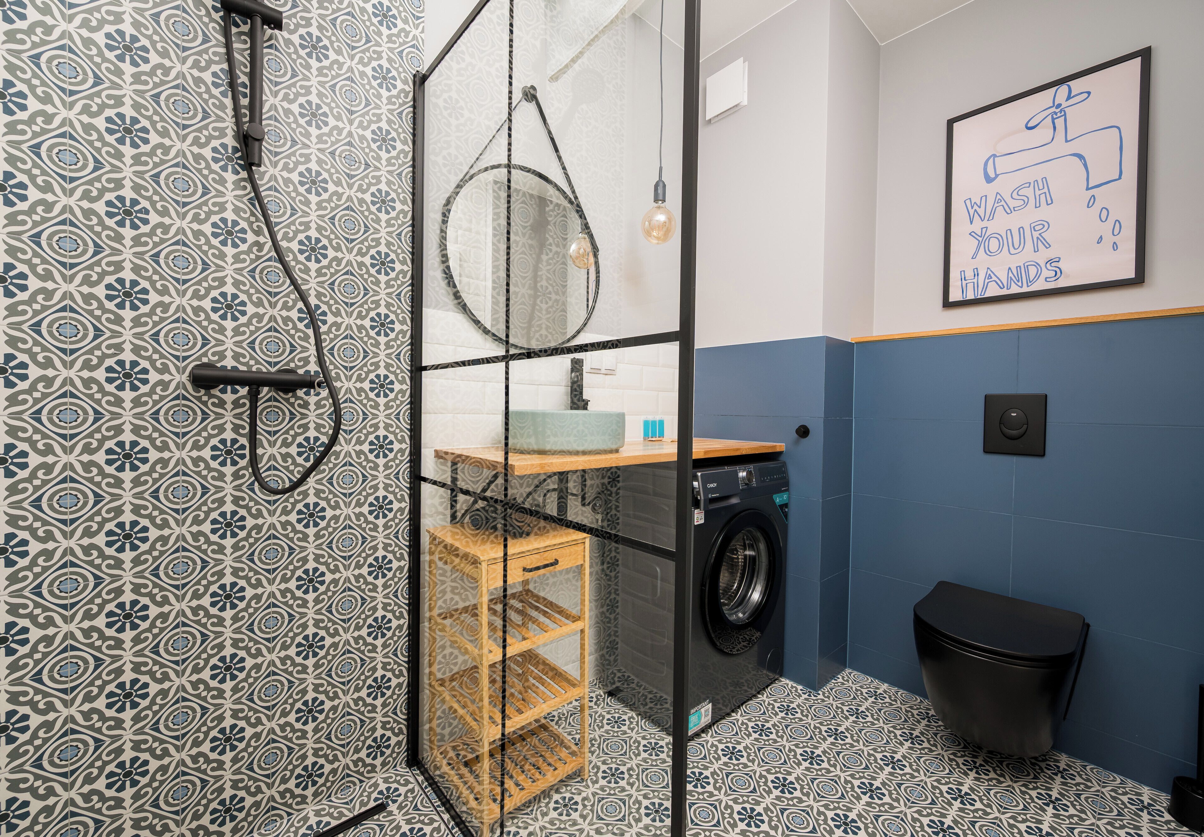 Une salle de bain moderne avec des carreaux à motifs, une douche en verre, un lave-linge et un panneau indiquant qu’il faut se laver les mains.