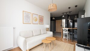A modern living room with a sofa, two small tables, a woven light fixture, and framed artwork on the wall. - Hemara Modern Apartment (Warszawa)