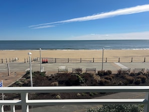 Blick auf einen Strand mit einer Promenade, Bänken und einer Brüstung.