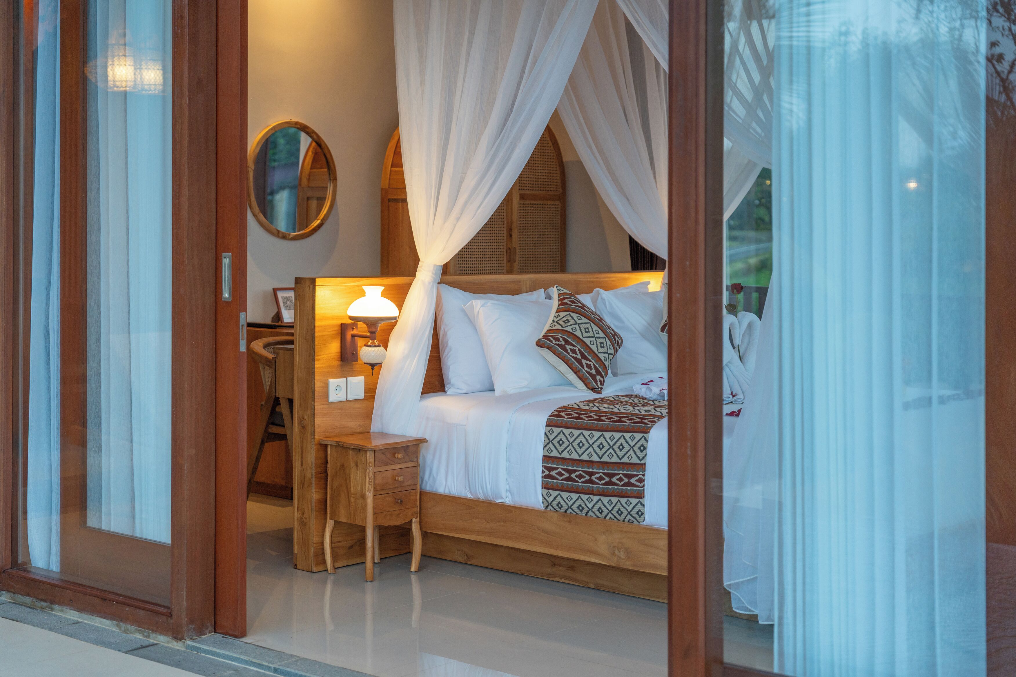 Une chambre à coucher avec un lit à baldaquin, une table de chevet, une lampe et un miroir au mur.