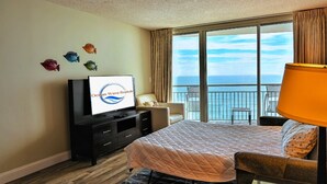 A hotel room with a bed, a TV, a chair, a desk, and a view of the ocean. - Stunning Oceanfront King Suite  at Oceans One Resort 8th Floor (Myrtle Beach)