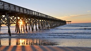 A pier extending into the ocean with the sun setting in the background. - Stunning Oceanfront King Suite  at Oceans One Resort 8th Floor (Myrtle Beach)