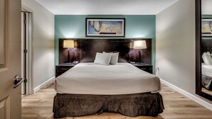 A hotel room with a large bed, a headboard with a painting, two bedside tables with lamps, and a mirror on the wall. - Stunning Oceanfront King Suite  at Oceans One Resort 8th Floor (Myrtle Beach)