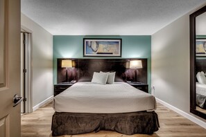 A hotel room with a large bed, a headboard with a painting, two bedside tables with lamps, and a mirror on the wall. - Stunning Oceanfront King Suite  at Oceans One Resort 8th Floor (Myrtle Beach)