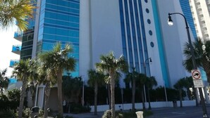 A tall hotel with a distinctive blue and white facade, palm trees in the foreground, and a clear blue sky. - Stunning Oceanfront King Suite  at Oceans One Resort 8th Floor (Myrtle Beach)