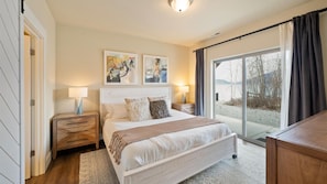 A bedroom with a bed, two bedside tables, a window with curtains, and artwork on the wall.