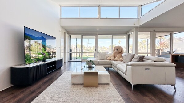 A modern living room with a large TV, a sectional sofa, and a view of the outdoors.