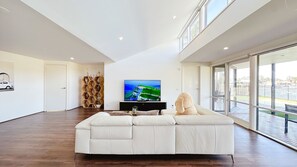 A spacious living room with a large flat-screen TV, a white sofa, and a wooden hexagonal shelving unit. - Lakefront/View/Swimming Pool/6B4B/Shopping Nearby (Patterson Lakes)