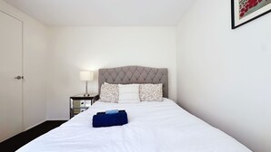 A neatly made bed with white bedding, a headboard with a diamond pattern, and a bedside table with a lamp. - Lakefront/View/Swimming Pool/6B4B/Shopping Nearby (Patterson Lakes)