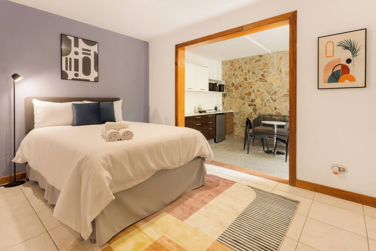 Une chambre à coucher avec un lit, une lampe de chevet et une vue sur la cuisine.