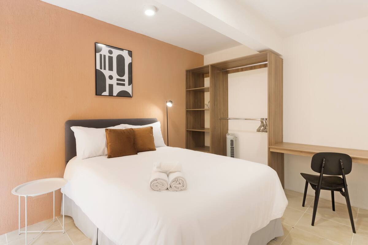 Une chambre d’hôtel équipée d’un lit, d’un bureau, d’une chaise, d’une armoire et d’une œuvre d’art accrochée au mur.