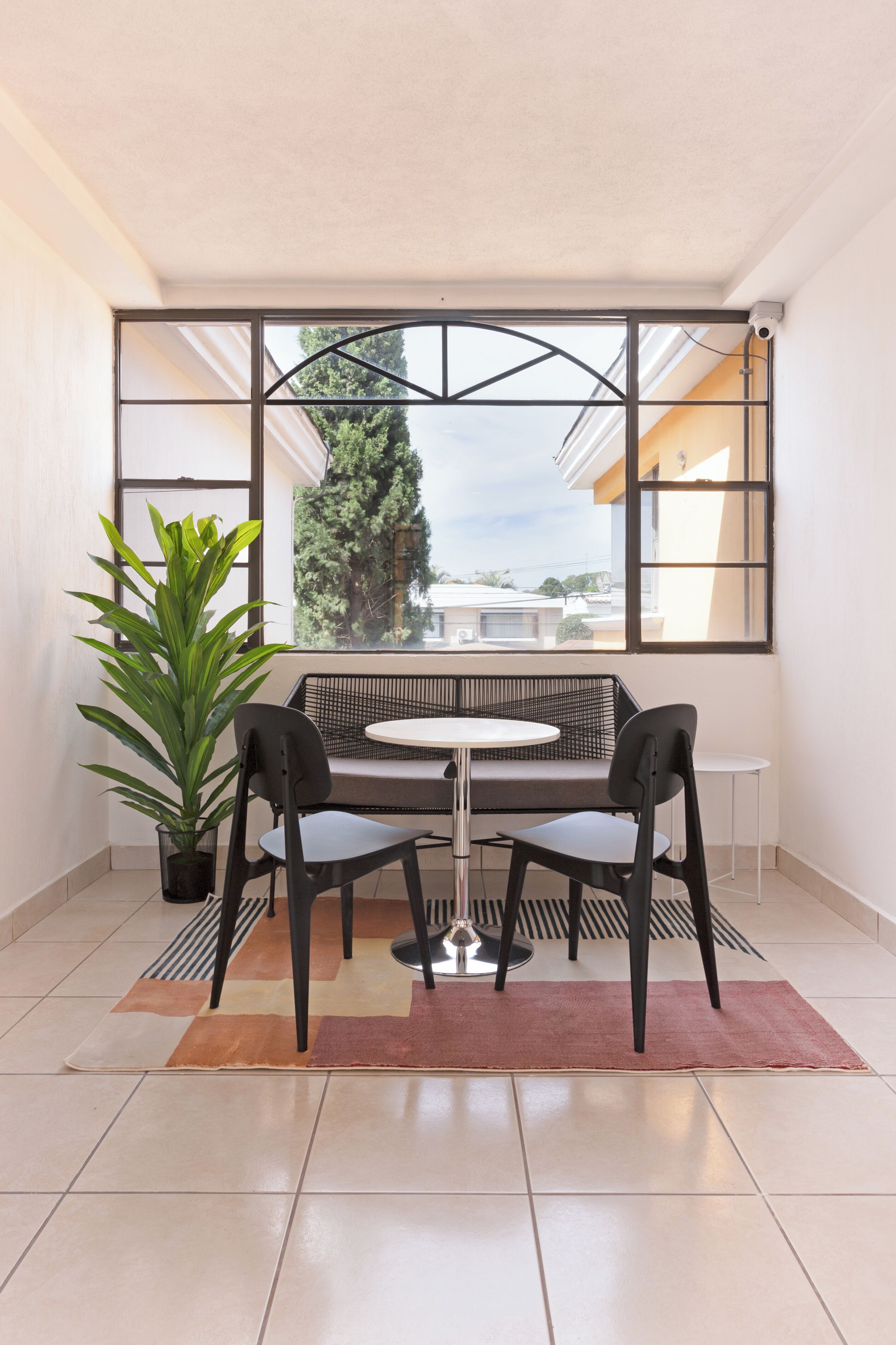Una habitación con un ventanal grande, una mesa redonda, dos sillas, una planta en maceta y un tapete a rayas.