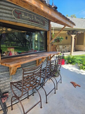 A rustic outdoor seating area with a wooden table and metal chairs, a sign reading 'Hooks 2 Horns Inc.', and a view of the surrounding landscape. - Salty Silo Bed & Breakfast, Breakfast upon request prior to arrival please! (Rockport)