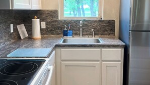 A kitchen with white cabinets, a stainless steel refrigerator, a window with a view of trees, and pendant lights. - Salty Silo Bed & Breakfast, Breakfast upon request prior to arrival please! (Rockport)