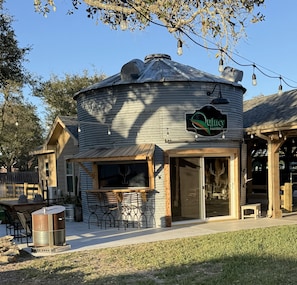 A rustic building with a round silo-like structure, a wooden sign, outdoor seating, and a patio area. - Salty Silo Bed & Breakfast, Breakfast upon request prior to arrival please! (Rockport)