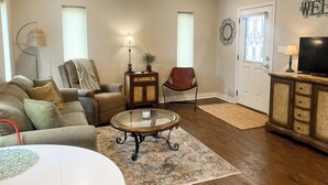 A living room with a sofa, armchair, coffee table, TV stand, and decorative wall art. - Salty Silo Bed & Breakfast, Breakfast upon request prior to arrival please! (Rockport)