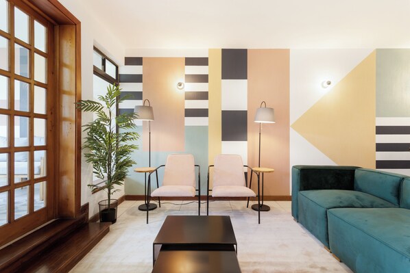 A modern living room with a sofa, two armchairs, a coffee table, a potted plant, and a large window with blinds. - Habiita13 Studio 101 (Guatemala City)