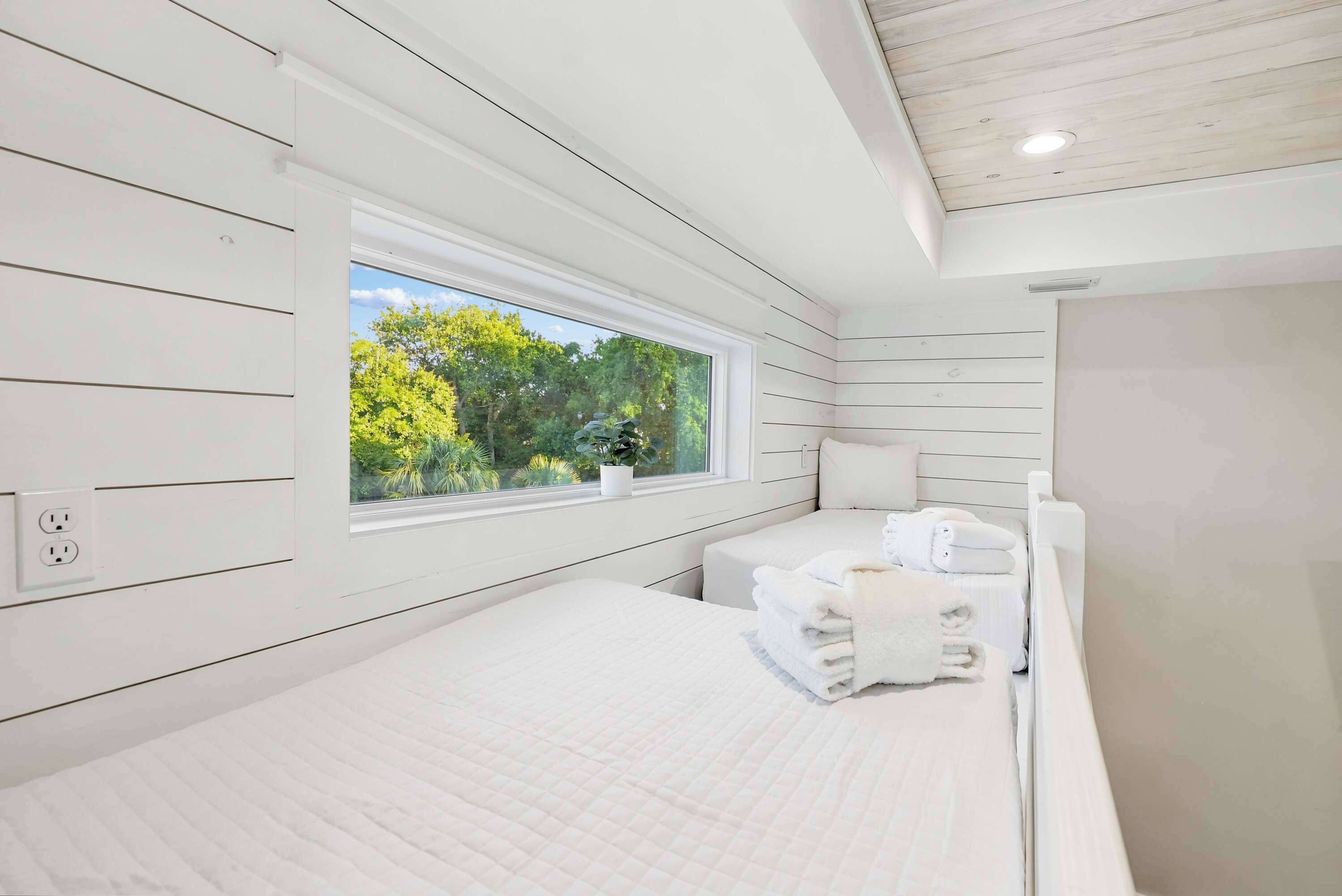 Ein Schlafzimmer mit einem großen Fenster, einem Bett, einem Nachttisch mit Handtüchern und einer weißen Decke.