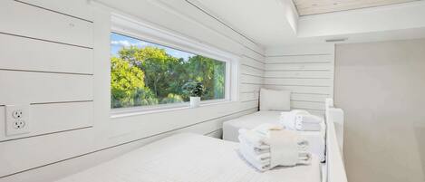 Ein Schlafzimmer mit einem großen Fenster, einem Bett, einem Nachttisch mit Handtüchern und einer weißen Decke.