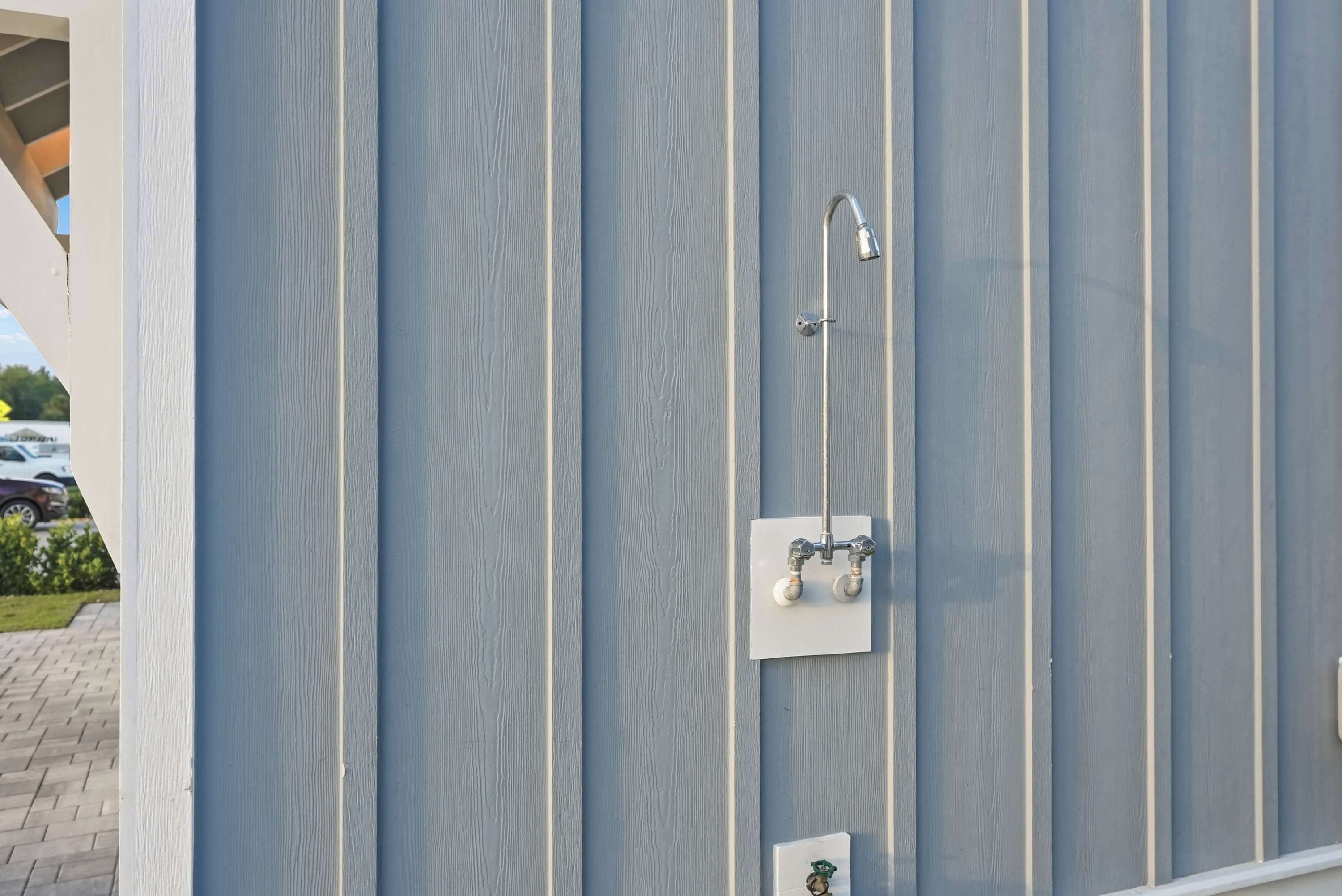A wall with vertical paneling, a showerhead, and two control valves.