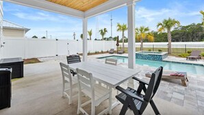 Une terrasse couverte avec une piscine, des meubles blancs et des palmiers.