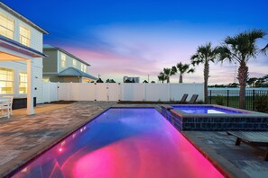 Ein Schwimmbad mit gefliestem Deck, ein eingezäunter Garten und ein zweistöckiges Haus mit Garage.