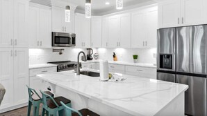 Une cuisine moderne avec des meubles blancs, des appareils en acier inoxydable et des luminaires suspendus.