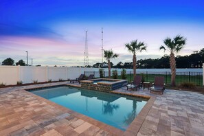 A swimming pool with a tiled deck, lounge chairs, palm trees, and a view of a body of water. - Panama Dunes & Shores | Sleeps 26 | 2 LSV | Pools (Panama City Beach)