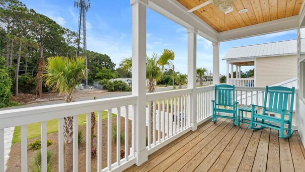 Une véranda couverte avec des balustrades blanches, deux chaises turquoise et un ventilateur de plafond.