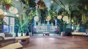 Ein Zimmer mit Holzboden, runden Tischen, hängenden Pflanzen und Korbmöbeln.
