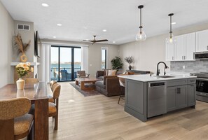 A modern kitchen with grey cabinets, a central island, and a dining area with a wooden table and chairs. - Viridian Bellevue - Luxury, roof top deck, private boat slip (Muskegon)