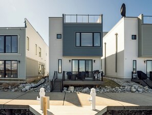 A modern multi-story residential building with a flat roof, large windows, and a covered outdoor seating area. - Viridian Bellevue - Luxury, roof top deck, private boat slip (Muskegon)