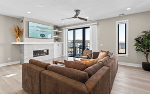 A living room with a fireplace, a ceiling fan, and a large window offering a view of the water. - Viridian Bellevue - Luxury, roof top deck, private boat slip (Muskegon)