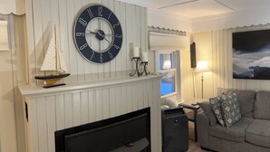 Una sala de estar con chimenea, un reloj grande, una maqueta de un velero, un sofá y un cuadro en la pared.