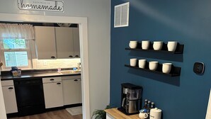 Una cocina con armarios blancos, una cafetera y un estante de pared con cuencos.