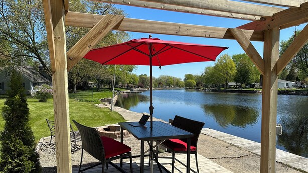 Una terraza de madera con una mesa, sillas y un paraguas rojo, con vista a un lago.