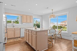 A modern kitchen with wooden cabinets, a central island, and a dining area with wicker chairs. - Welcome to Selah by the Sea, your perfectly located Bald Head Island escape (Bald Head Island)