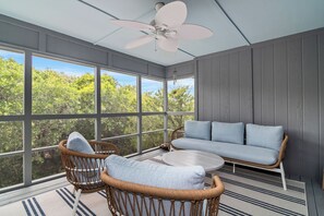 A sunroom with wicker furniture, a ceiling fan, and large windows offering a view of greenery. - Welcome to Selah by the Sea, your perfectly located Bald Head Island escape (Bald Head Island)