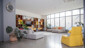Een ruime woonkamer met een moderne bank, een gele fauteuil en een grote boekenkast.