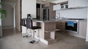 Een moderne keuken met een centraal eiland, barstoelen, roestvrijstalen apparatuur en een betegelde spatwand.