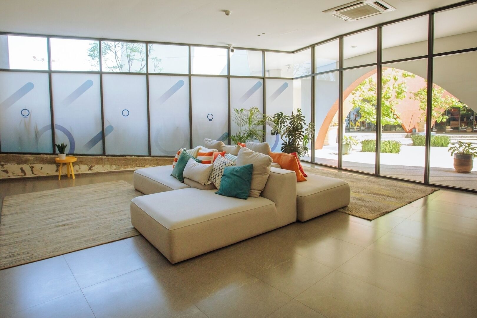 Um interior moderno com um sofá modular, janelas amplas e plantas dentro de casa.